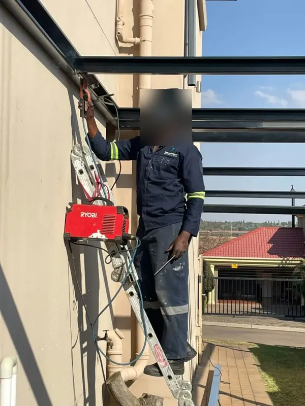 Member of the Bheki team welding a steel frame against the side of a house